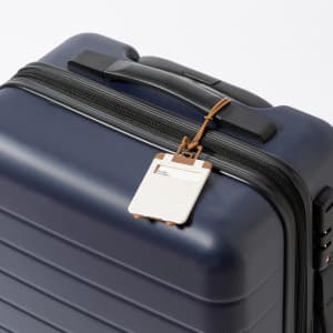 A navy luggage tag attached to a sleek dark suitcase, featuring a simple outline and a leather loop.