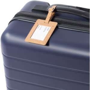 A navy suitcase with a beige luggage tag attached, featuring a leather look and a blank area for personal details.