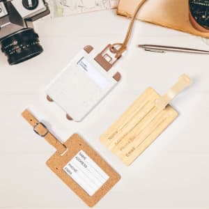 Three luggage tags displayed: a white tag with a brown strap, a cork tag with a clear strap, and a wooden tag with a brown strap.