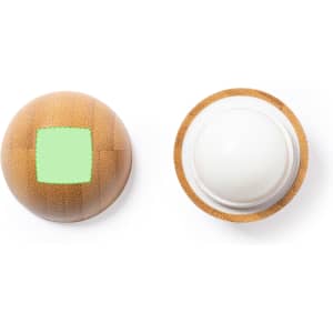 A round lip balm in a natural textured container with a green square. The balm is white and has a logo on the base.