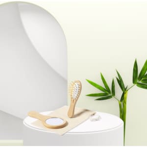 A bamboo hairbrush and mirror set displayed on a cloth, with green bamboo leaves in the background.