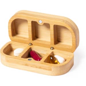 A wooden pillbox with three compartments containing various capsules and tablets. It features a logo.