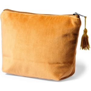 A soft, orange velvet toiletry bag with a zip closure and a decorative tassel. Features branding on the side.