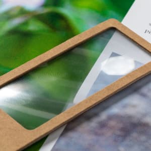 A magnifier bookmark with a transparent lens and a light brown cardboard frame, resting on printed paper.