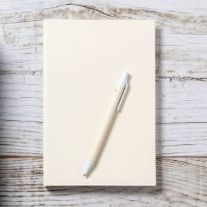 A cream notebook with a white Roliok pen resting atop it on a rustic wooden surface.