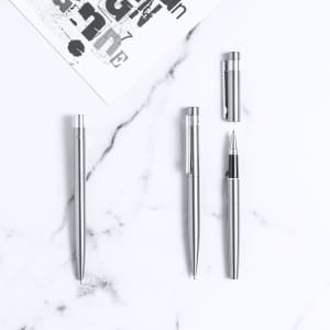 A set of silver metal pens displayed on a marble surface, featuring a branding logo.