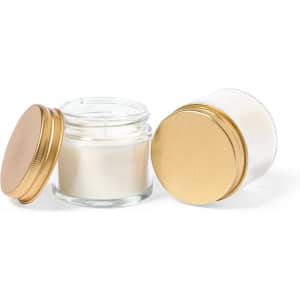 A set of two candles in glass jars with gold lids, featuring a white wax interior.