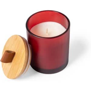 A red aromatic candle in a glass container with a wooden lid. The candle is unlit and features a wick.