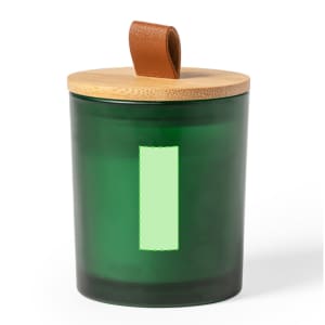 A green aromatic candle in a glass container with a wooden lid and a leather strap.