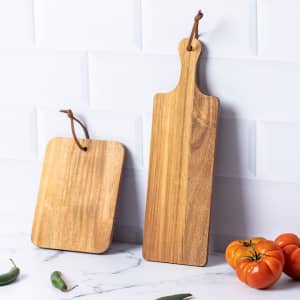 Two wooden cutting boards in natural tones, one rectangular and one square, with hanging loops against a white backdrop.