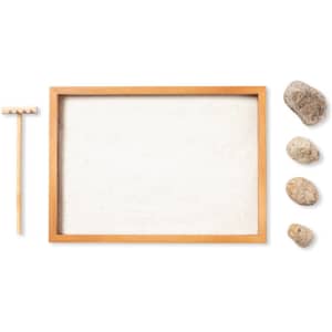 A mini zen garden with a wooden frame, white sand, a small rake, and four decorative stones.
