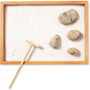 A mini zen garden featuring a wooden frame, white sand, smooth rocks, and a small rake.