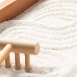 A mini zen garden featuring white sand and a wooden rake, set within a wooden frame.