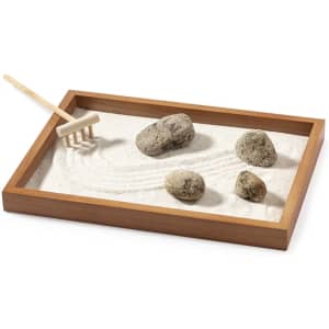 A wooden tray filled with white sand, featuring smooth stones and a small rake for gardening.