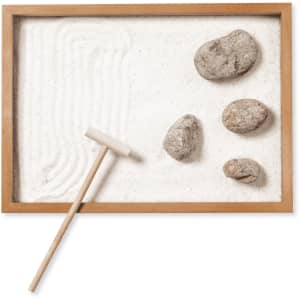 A wooden-framed mini zen garden with white sand, smooth stones, and a rake for patterns.