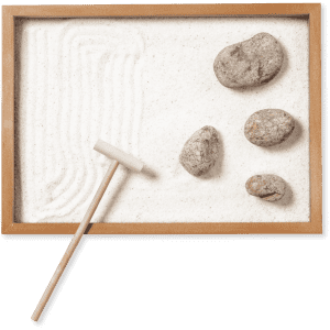 A wooden mini zen garden with white sand, four grey rocks, and a small rake.