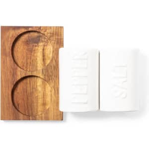 A wooden holder with two white salt and pepper shakers. The shakers are cylindrical with embossed labels.
