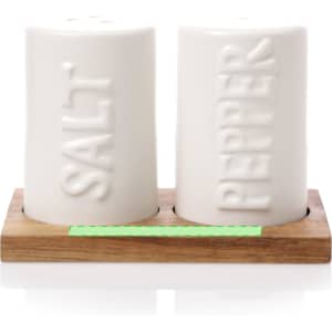 A white salt and pepper shaker set sits on a wooden holder, featuring raised text.