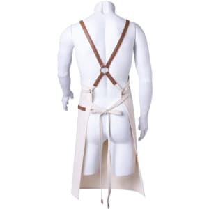 A beige apron with brown leather straps is displayed from the back on a mannequin. The apron features a tie detail.