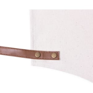 A cream apron with a brown leather strap featuring two brass buttons and a textured fabric.