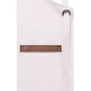 A cream apron featuring a brown leather patch and a white strap. The apron has a subtle, textured fabric.