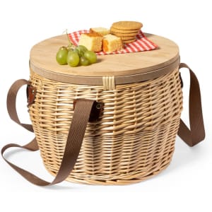 A woven thermal picnic basket in natural tones, featuring a wooden lid, carrying straps, and snacks on top.