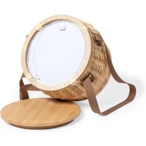 A woven, round thermal picnic basket in natural tones with a brown strap and a wooden lid. It features a clear plastic top and has a logo.