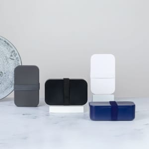 A collection of Sandix Lunch Boxes in grey, black, white, and navy, each with a band and minimalist design.