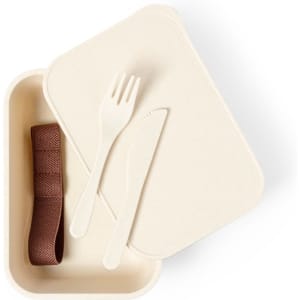 A cream-coloured lunch box with a fork, knife, and a brown elastic band inside. It has a simple design.