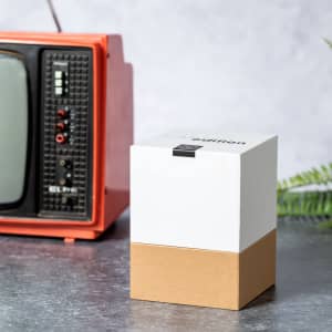 A white and brown box with a lid, placed beside an orange vintage television on a grey surface.