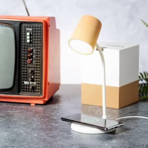 A multifunction lamp with a beige shade and white base, positioned on a desk next to a retro television.