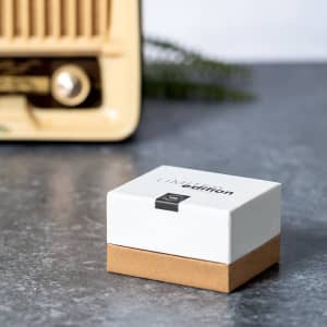A box of Crawly Earphones in white and brown, set against a vintage radio on a grey surface.