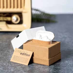 A pair of white earbuds in a brown and white box, set against a textured grey surface. The packaging features a logo.