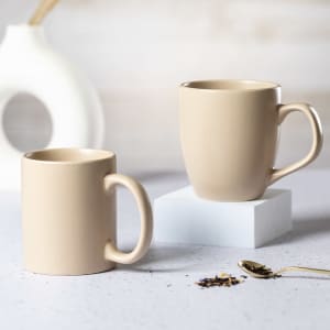 Two beige coffee mugs are positioned on a white pedestal, with one mug slightly larger than the other.