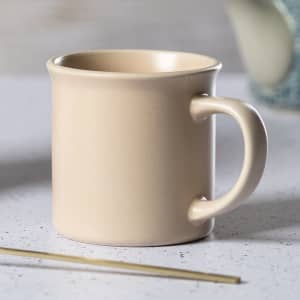 A coffee mug in a soft beige colour with a simple design and a rounded handle.