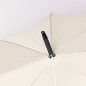 A beige umbrella featuring a black handle, with a sleek design and a central tip component.