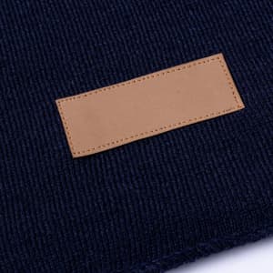 A dark navy scarf with a textured knit pattern and a beige leather label patch.