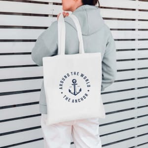 A cream tote bag with an anchor design and a logo, being carried by a person.