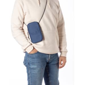 A navy multipurpose bag with a strap is worn across the body, paired with a light hoodie and jeans.
