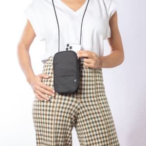 A black multipurpose bag is worn crossbody, held in one hand, featuring a logo and worn with patterned trousers.
