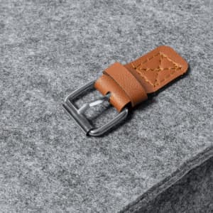 A grey felt surface features a brown leather strap with a silver metal buckle.