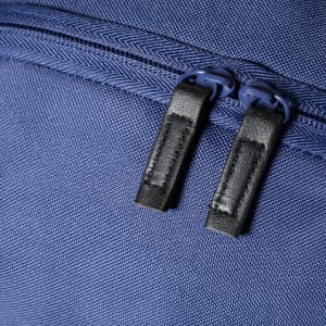 A close-up of a blue backpack fabric featuring black zippers with leather pulls. The material has a textured pattern.