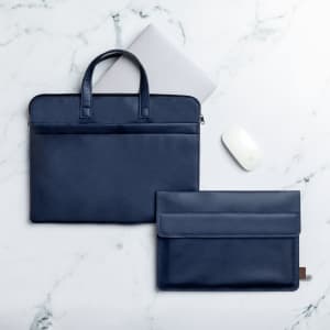 A navy document bag and a smaller matching pouch are placed on a marbled surface, alongside a laptop and a mouse.