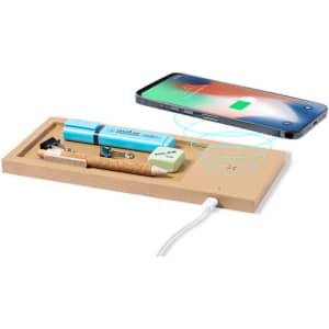 A wooden wireless charger with a light blue organiser holding pens and a notepad, next to a smartphone charging.