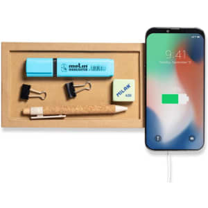A wireless charger in light wood finish with a phone, a blue highlighter, a pencil, sticky notes, and binder clips.