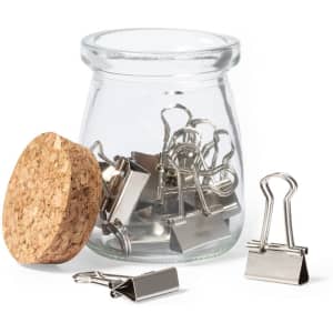 A glass jar containing silver metal binder clips, with a cork lid partially removed.