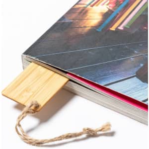 A bamboo bookmark with a twine attachment inserted into a colourful book. The book cover is vibrant and textured.