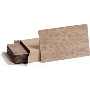 A set of brown wooden business cards presented in a kraft paper holder. The cards have a textured finish.
