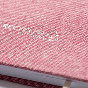 A pink notepad with a textured cover and a logo, featuring recycled material branding.