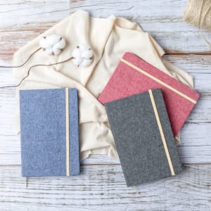 Three notepads in blue, grey, and pink, with wooden accents, placed on a light fabric background.